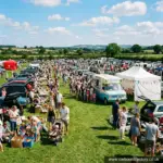 Sunny bank holiday car boot sale with families browsing stalls and a queue at the ice cream van